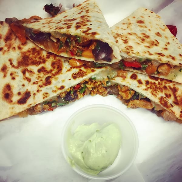 Chicken quesadillas with black beans, peppers, and onions, served with a side of guacamole.
