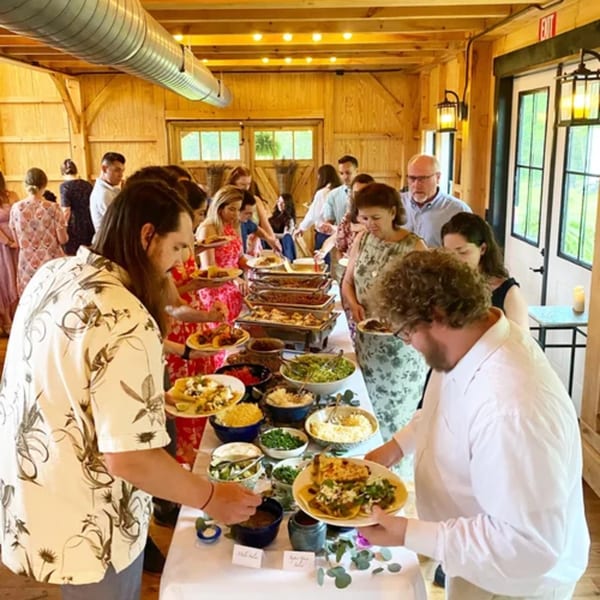 Guests serving themselves Mexican food from a buffet line in a rustic, warmly lit barn.
