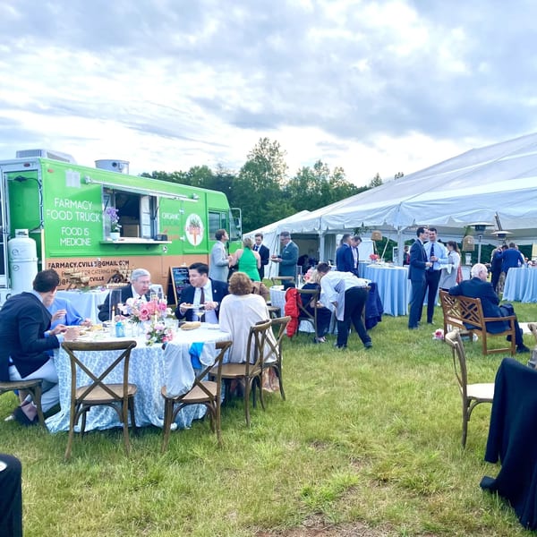 Guests dine outdoors at tables with a Farmacy Cafe food truck and large white tent in the background.