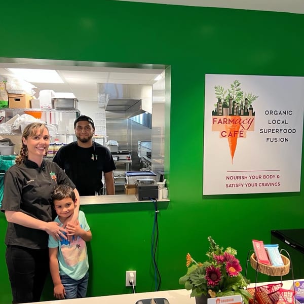 Farmacy Cafe staff, a woman and a man, with a child in front of the kitchen pass-through.