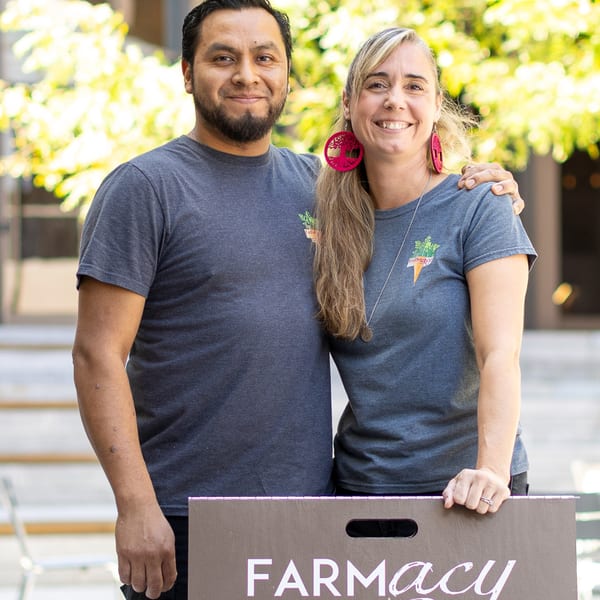 Two smiling Farmacy Cafe owners, a man and a woman, stand together holding a sign.