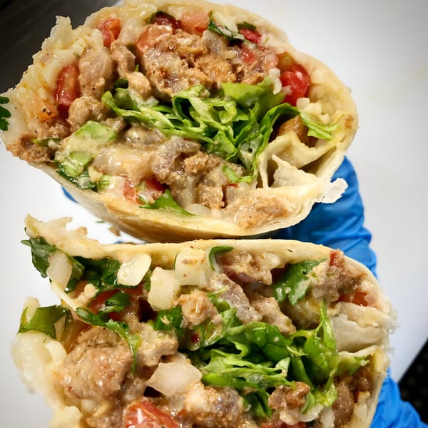 A Farmacy Cafe Mexican burrito, cut in half, revealing meat, lettuce, tomatoes, and sauce.