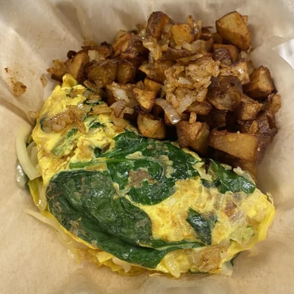 A Farmacy Cafe breakfast burrito with scrambled eggs, spinach, and roasted potatoes in a paper-lined basket.