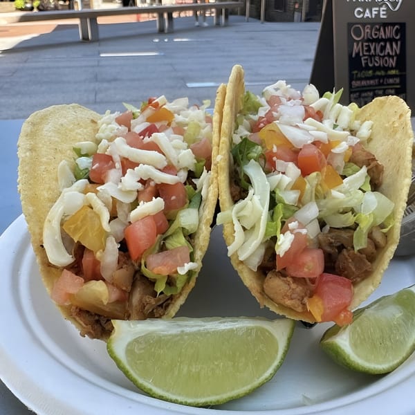 Two Farmacy Cafe organic Mexican fusion tacos with chicken, lettuce, tomatoes, cheese, and lime wedges.