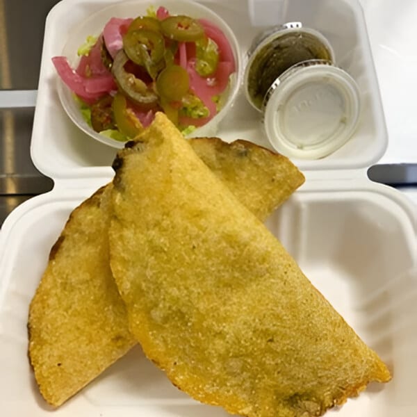 Two golden-brown empanadas with a side of pickled onions, jalapeños, and two sauce containers.