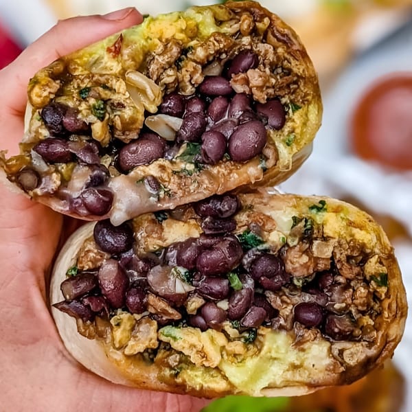 A hand holds a Farmacy Cafe burrito, cut in half, revealing black beans, scrambled eggs, and cheese.