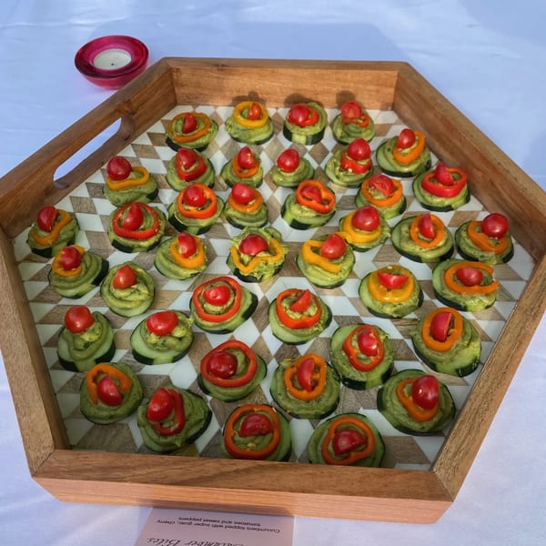 A wooden tray filled with Farmacy Cafe's cucumber bites topped with guacamole, cherry tomatoes, and sweet peppers.