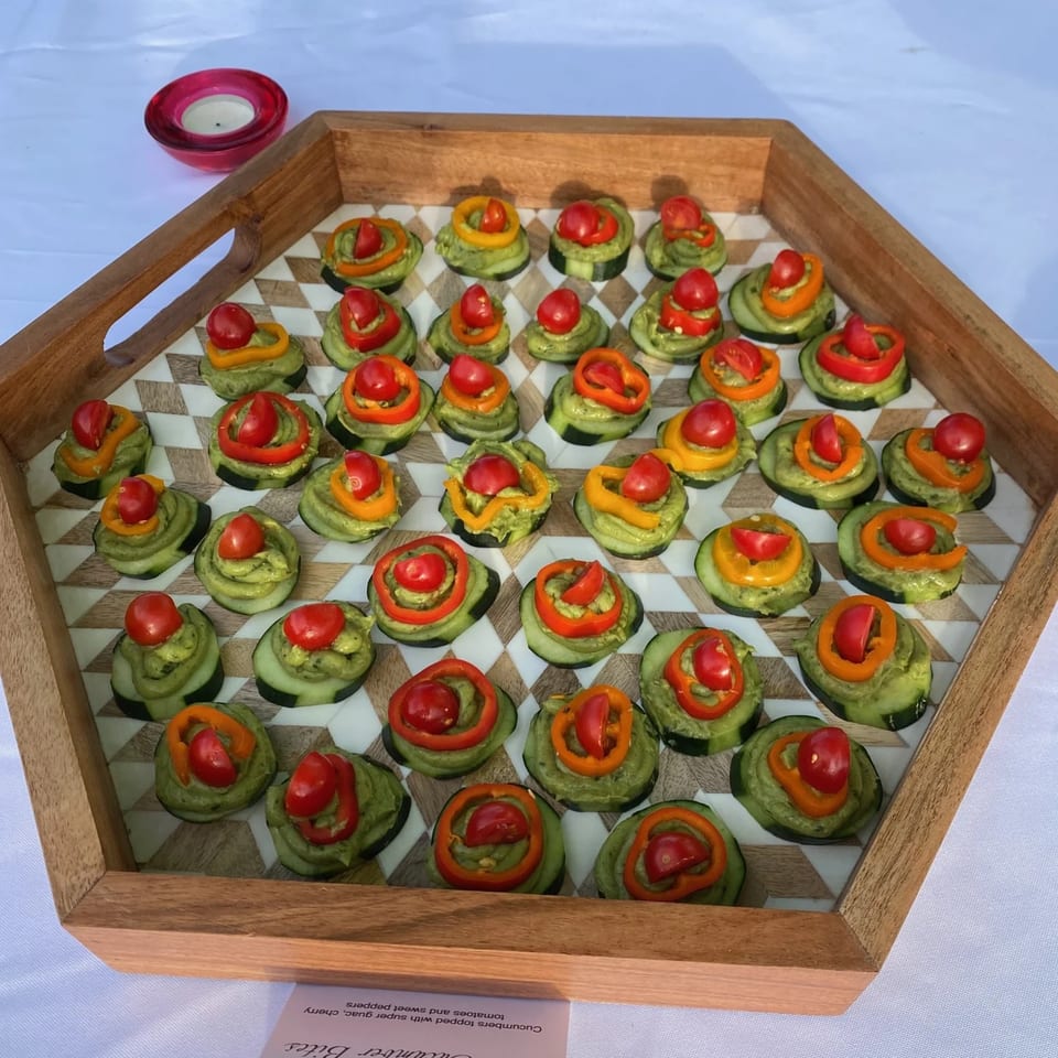 A wooden tray filled with Farmacy Cafe's cucumber bites topped with guacamole, cherry tomatoes, and sweet peppers.