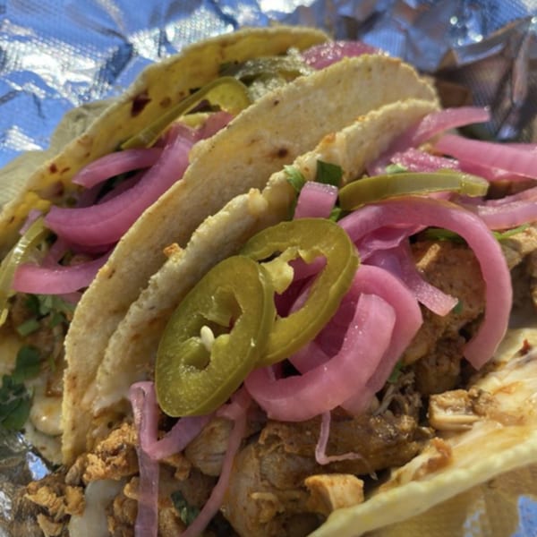 Three Farmacy Cafe tacos filled with meat, pickled red onions, and jalapeños, wrapped in foil.