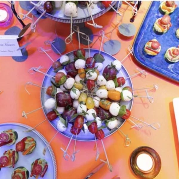 Colorful skewers with cherry tomatoes, mozzarella balls, and basil leaves on a blue plate.