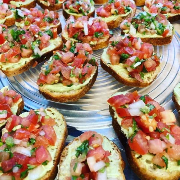 Close-up of numerous avocado toast bites topped with fresh diced tomatoes, onions, and cilantro.