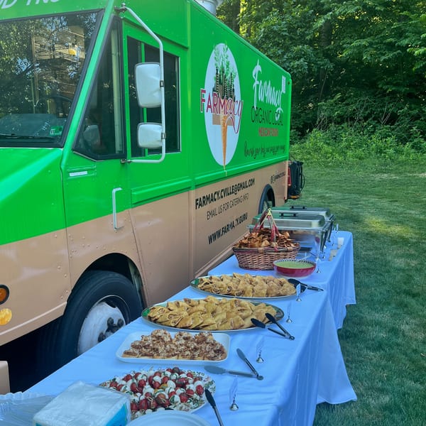 A Farmacy food truck with a catering table displaying various dishes, including chips, guacamole, and skewers.